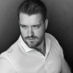 Porträt von Hoellety mit kurzem Haar und Bart, der direkt in die Kamera schaut, vor einem Schwarzen Hintergrund.